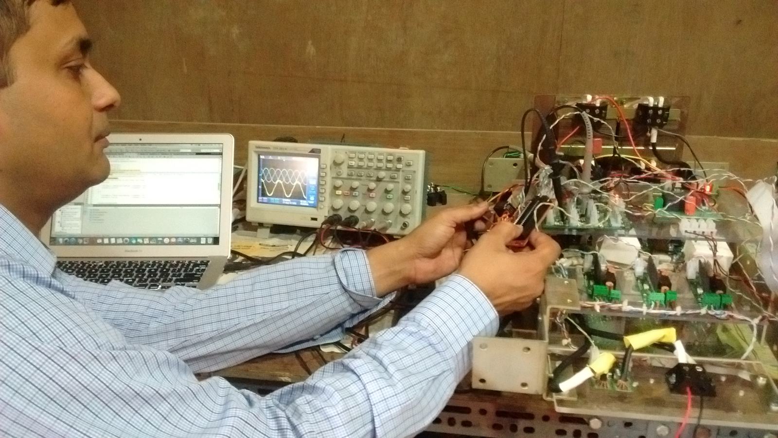 Engineer adjusting wiring on a power board with an oscilloscope and laptop on the bench