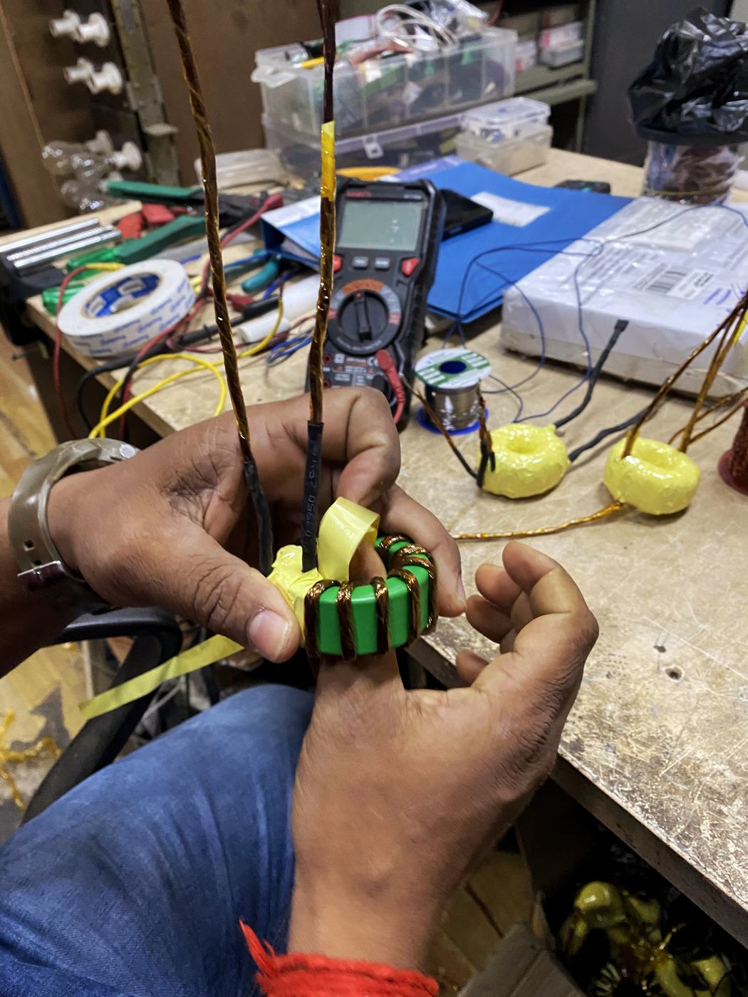 Hands holding a hand-wound toroidal choke while a multimeter reads its values