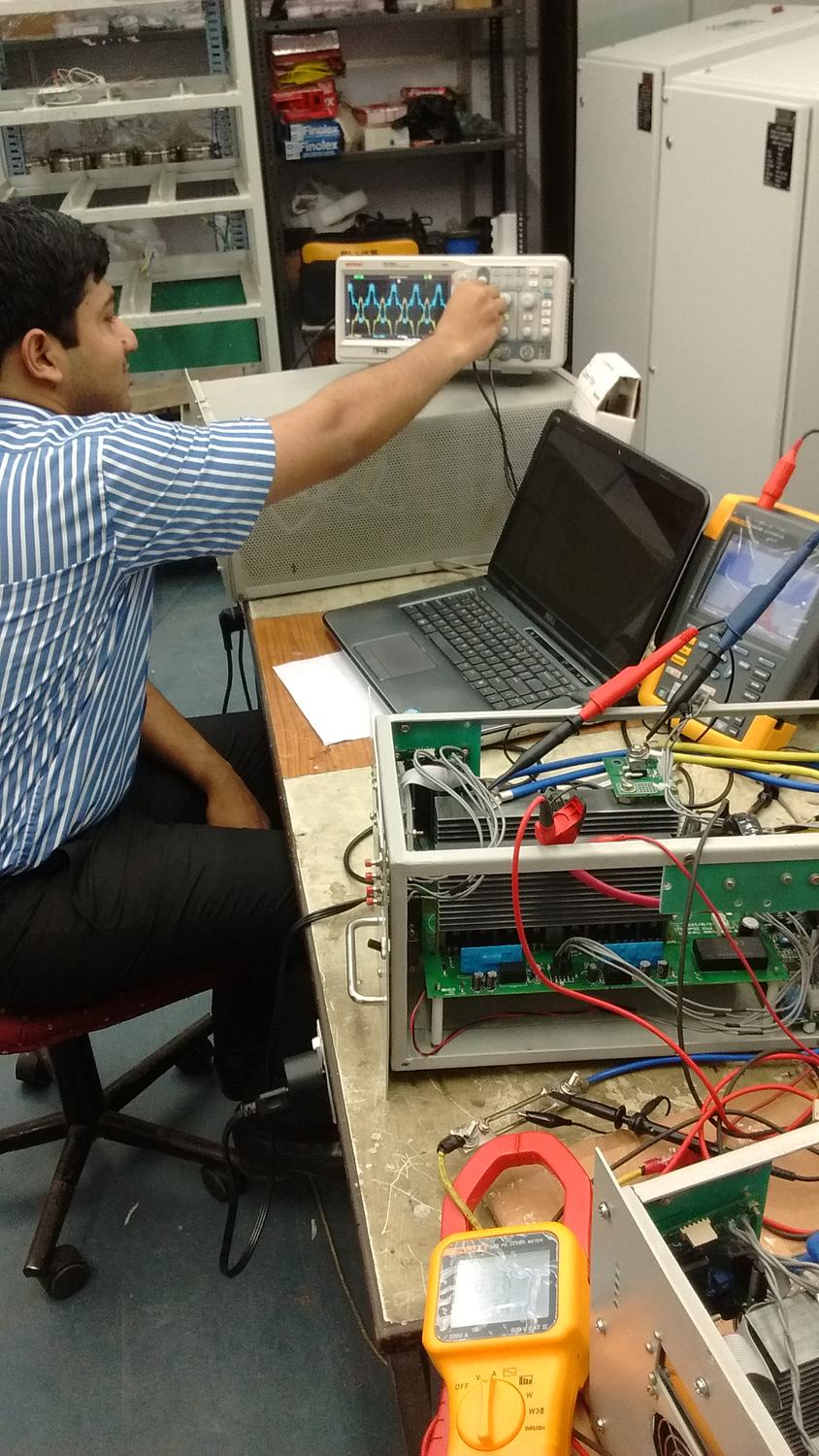Engineer at an oscilloscope beside a power board wired to a clamp meter and laptop